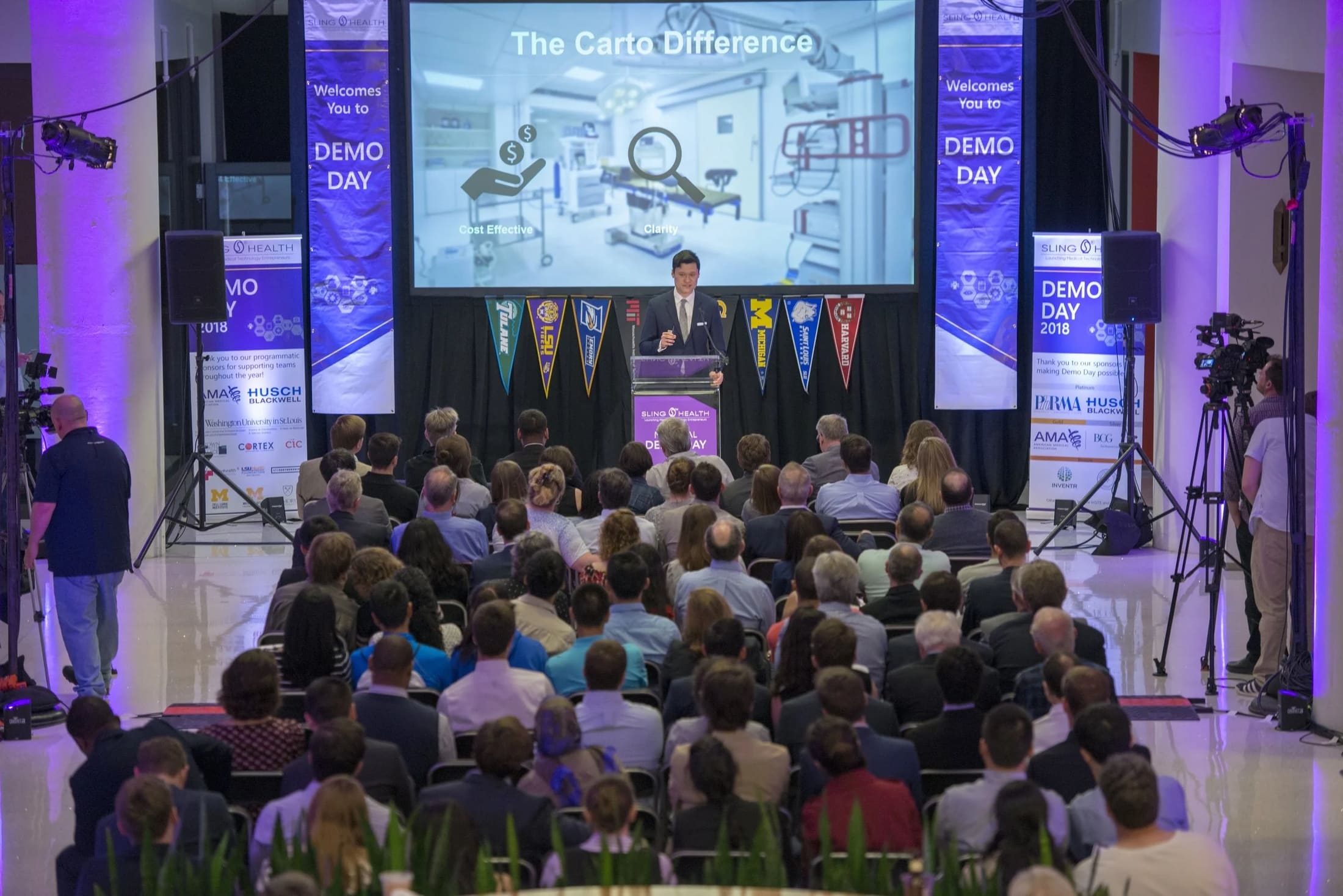 A full Sling Health Demo Day auditorium with sponsor banners lining the stage.